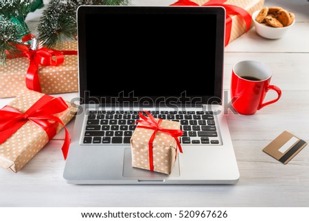 Christmas online shopping. Laptop with copy space on screen lay on white wood, present boxes and christmas tree on background. Internet commerce on winter holidays concept