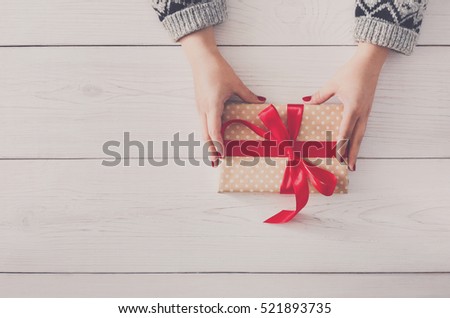 Woman\'s hands give wrapped christmas or other holiday handmade present in paper with red ribbon. Present box, decoration of gift on white wooden table with copy space