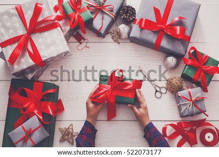 Creative diy hobby. Wrapping modern handmade christmas present, boxes in stylish paper with satin red ribbon. Top view of hands on messy white wood table with fir tree branches, decoration of gift.