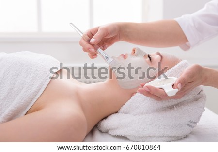 Face peeling mask, spa beauty treatment, skincare. Woman getting facial care by beautician at spa salon, side view, close-up