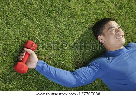 Young Athletic Man Lying Down in Grass with Dumbbells, Close Up