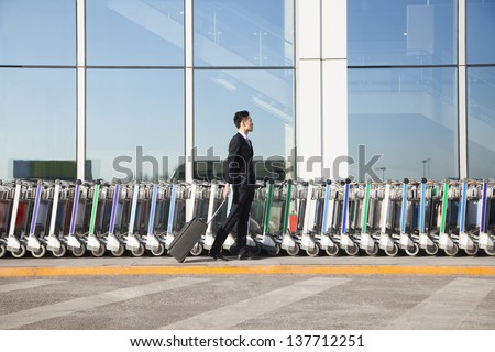 Traveler with suitcase next to row of luggage carts at airport