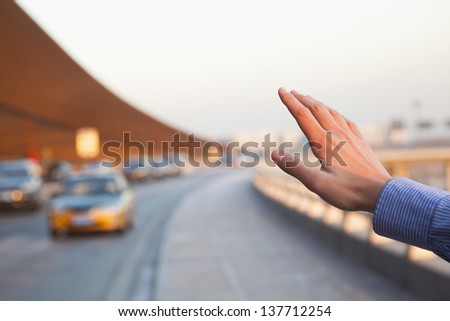 Hand of traveler hailing a taxi outside of the airport