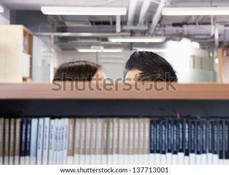 Work romance between two business people hiding behind shelves