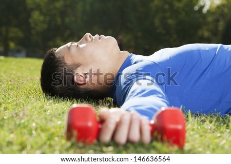 Young Athletic Man Lying Down in Park with Dumbbells