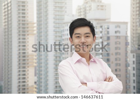 Portrait of young businessman in button down shirt with arms crossed, skyscraper in background