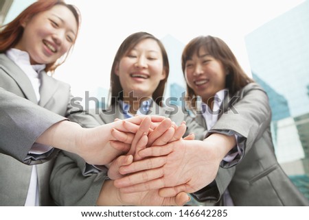 Three young businesswomen putting hands together, low angle view