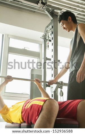 Young men weight lifting with his personal trainer in the gym