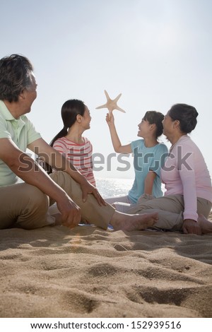 Multi generational family sitting on the beach looking at starfish