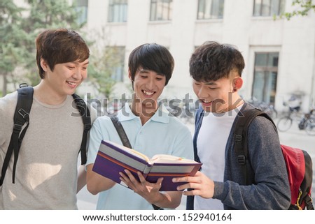 Three students discussing and looking at the book