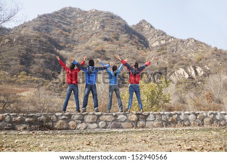 Group of young people standing on the ledge, arms outstretched