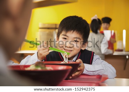 School boy eats noodles in school cafeteria