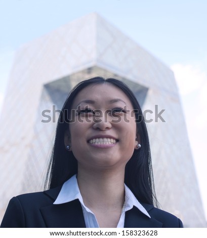 Portrait of smiling young businesswoman with the CCTV building in background