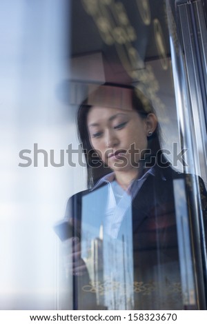 Young businesswoman using phone on the other side of glass window
