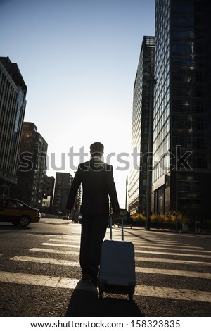Rear view of young Businessman walking down the street with luggage