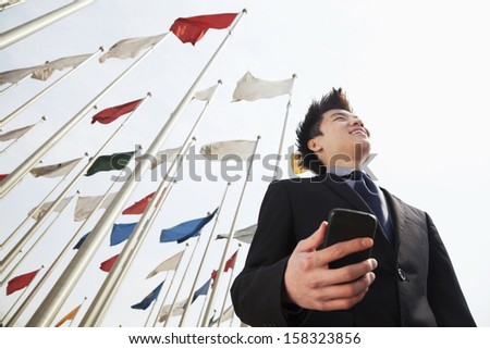 Smiling young businessman holding phone with flags in the background