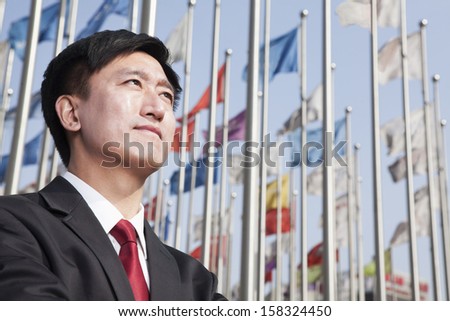 Businessmen looking away with flagpoles in background.