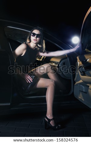 Young elegant woman stepping out of the car in sunglasses