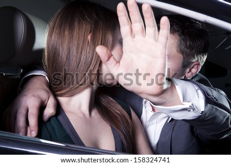 Young couple kissing in car and man is shielding with his arm