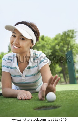 Smiling young woman flicking the golf ball into the hole