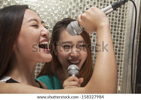 Two young female friends singing into microphone at karaoke