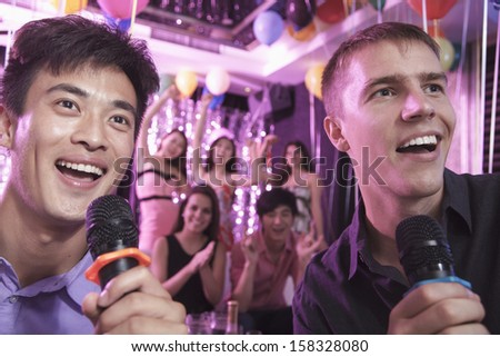 Two friends holding microphones and singing together at karaoke