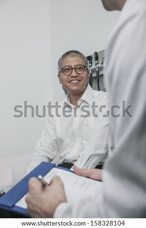 Doctor writing on medical chart with a smiling patient