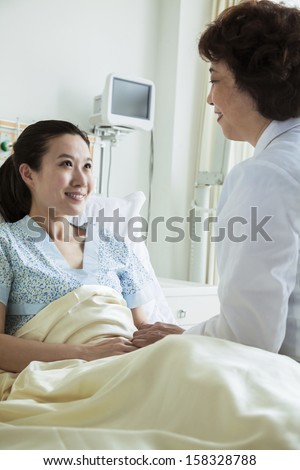 Female doctor sitting on hospital bed and discussing with young female patient