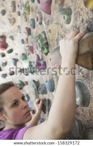 Determined young woman climbing up a climbing wall
