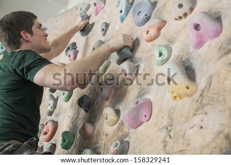 Determined young man climbing up a climbing wall