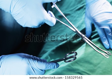 Close-up of gloved hands holding surgical scissors and working