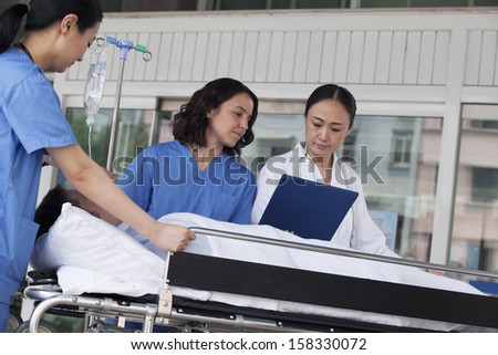 Paramedics and doctor looking down at medical record of patient on a stretcher