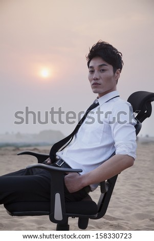 Businessman sitting on a chair and looking at camera in the middle of the desert