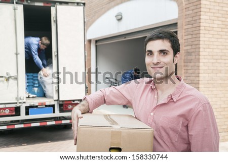 Smiling man holding a cardboard box and moving into his new home