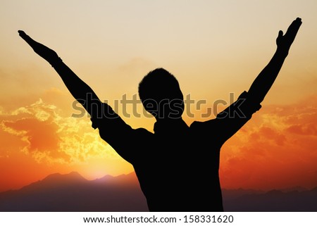 Silhouette of young man with arms raised with beautiful sunset and landscape in background