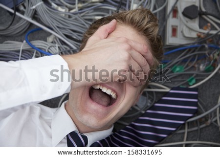 Frustrated man lying down covering his eyes surrounded by computer cables