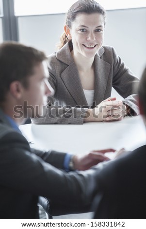 Three smiling business people sitting at table and having business meeting in the office