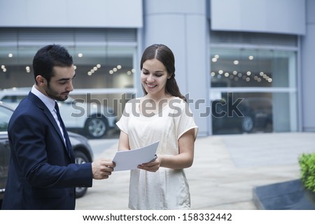 Car salesman and young woman looking over paperwork