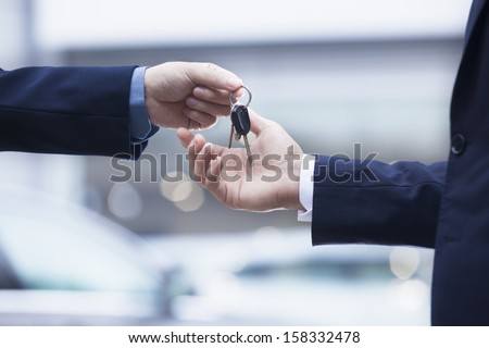 Car Salesman Handing Over The Keys For A New Car To A Young Businessman