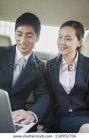 Business colleagues using laptop in back seat of car