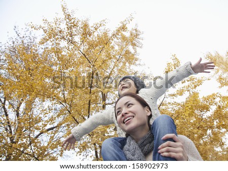 Mother and daughter with arms outstretched and surrounded by autumn trees