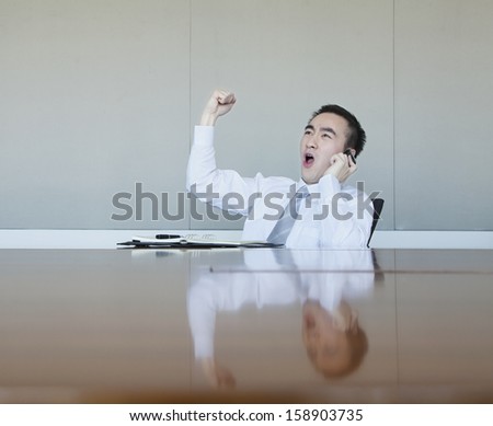 Young businessman with fist in air talking on phone