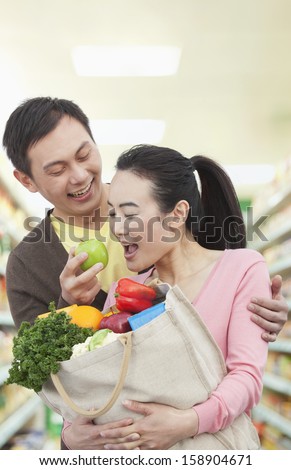 Man feeding woman with apple in grocery store