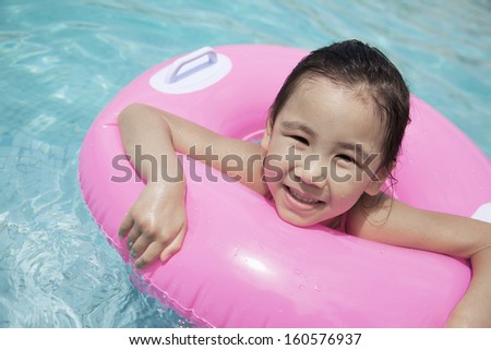 Portrait of cute little girl swimming in pool with pink tube