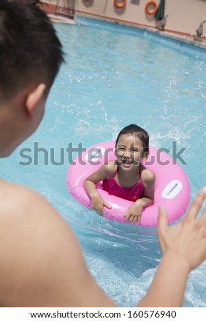 Little girl with pink tube and her father swimming in pool