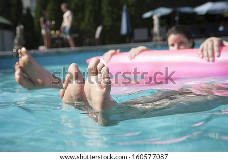 Low section of two friends in pool holding onto  inflatable raft with feet sticking out of  water