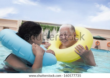 Senior couple smiling and relaxing in pool with inflatable tubes
