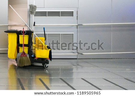 Yellow cleaning trolley park in walkway on stainless wall background.