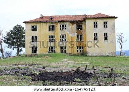 Haunted abandoned building of old public school with no windows on green hill. Horror and after war concept.