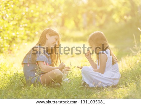 Two little girls in dresses sitting on the grass in the park and playing rock paper scissors hand game